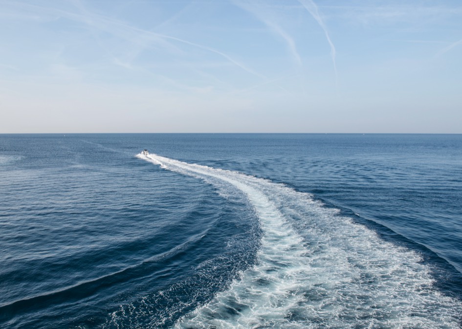 slightly aerial view of a boat's wake on a vast body of water, likely the ocean