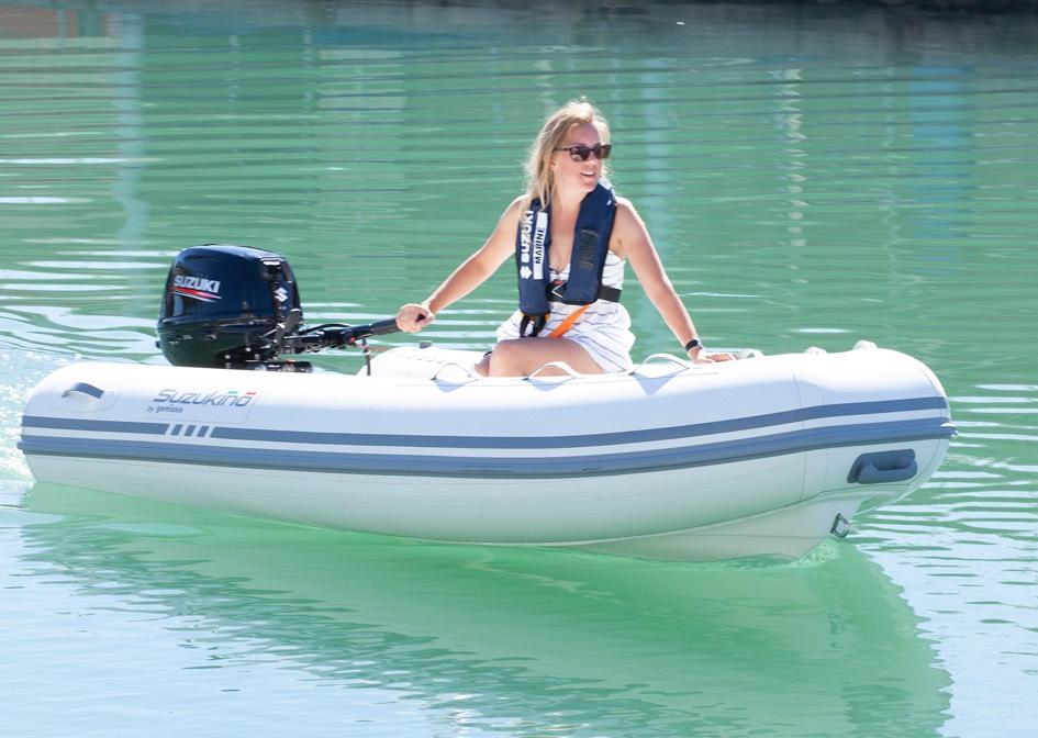 A small white inflatable boat, anchored in shallow water, glides smoothly with a Suzuki outboard engine.